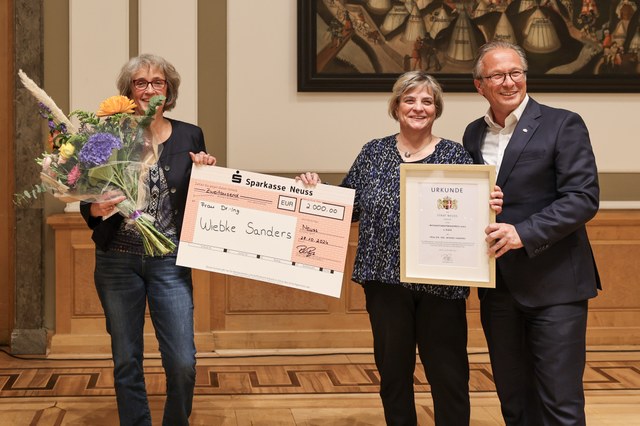IFP_07.jpg Die Preisträgerin hält einen Blumenstrauß in der Hand und zeigt gemeinsam mit dem Bürgermeister einen symbolischen Scheck sowie die Urkunde in die Kamera.